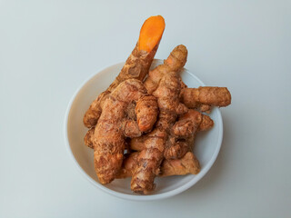 Turmeric or Curcuma longa rhizomes in a bowl, isolated in white background