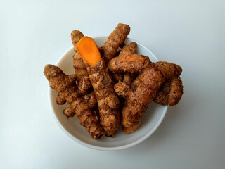 Turmeric or Curcuma longa rhizomes in a bowl, isolated in white background