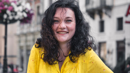 Portait of Beautiful Young Lady Wearing Yellow Dress Curly Hair Looking Happy. Young Attractive  woman smiling happy and confident. Standing at town street.