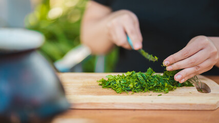 Woman cutting greens on wooden board outdoors. Close up of woman's hands cutting verdure with knife on chopping board.