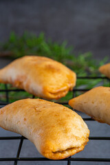 Close up view on homemade freshly baked empanadas pastry with meat filling a gluten-free version of an authentic traditional Spanish Latin America cuisine food on a black cooling rack
