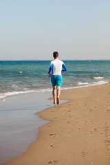 Fototapeta na wymiar A male athlete runs along the beach in blue shorts along the sea. Coast of Cyprus. Copy space.