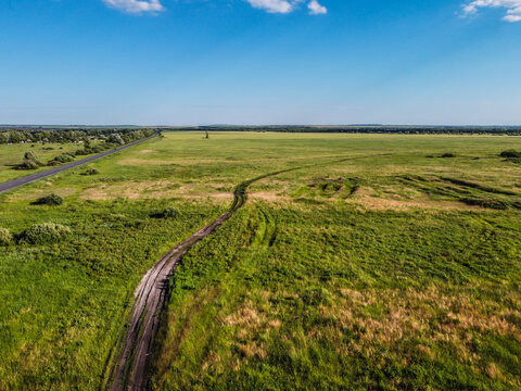 aerial view over field with green grass and empty gravel road during sunny summer day, Samara region, Russia