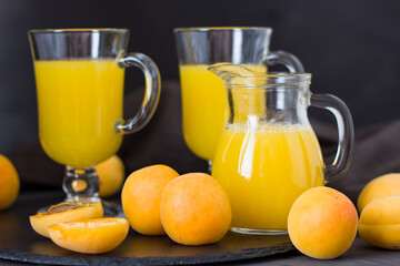 Fototapeta premium Apricot juice is poured into a glass. Apricots with a white plate. Dark background.