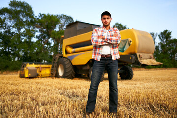 Portrait of proud harvester machine driver with hands crossed on chest. Farmer standing at his...