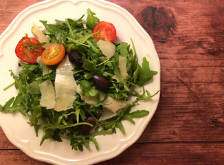 Arugula salad with sliced parmesan cheese, cherry tomatoes and olives.