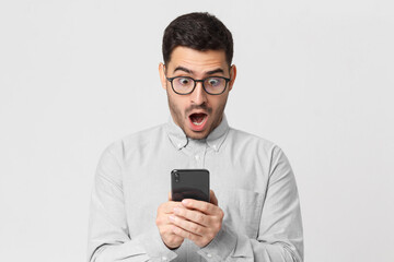 Shocked business man in casual shirt looking at his phone with surprise expression, isolated on gray background