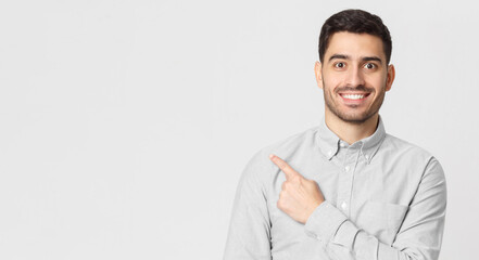 Banner of excited young man in shirt pointing with finger to left side, isolated on gray background with copy space