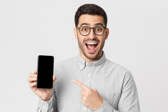 Excited business man in casual shirt showing his phone with blank screen, shouting WOW, isolated on gray background