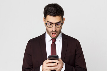 Shocked business man looking at his smartphone with surprise OMG expression, isolated on gray background - obrazy, fototapety, plakaty
