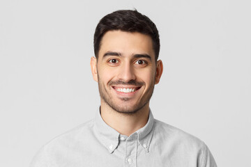 Close up portrait of young smiling handsome man wearing gray shirt, feeling confident as...