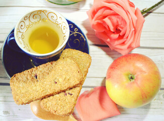 Green tea cup with a beautiful rose and cereal cookies on the table for healthy and romantic breakfast or lunch. Closeup. 