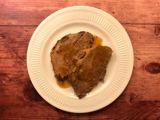 Roast pork with gravy on white plate. 