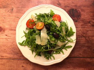 Arugula salad with sliced parmesan cheese, cherry tomatoes and olives.