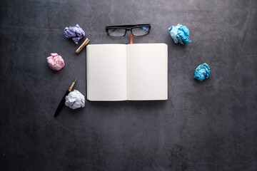 Journalist's table with notebook, crumpled paper on black background.