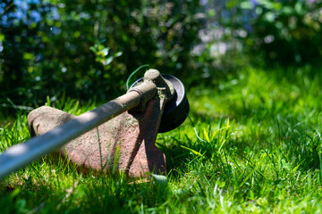 a grass trimmer lies flat on the  grass in the shade on a hot summer day