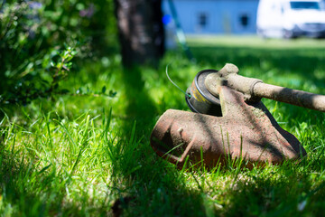a grass trimmer lies flat on the  grass in the shade on a hot summer day