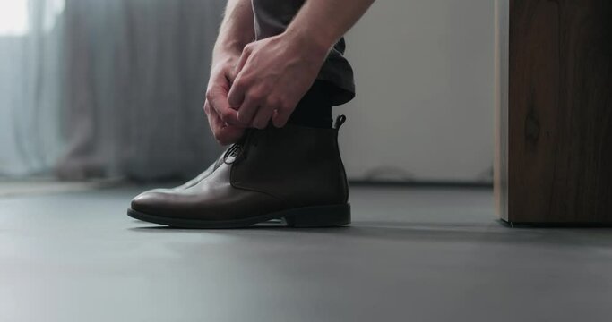 Slow motion man unlace his brown leather chukka boots indoor