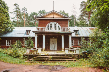 An old wooden noble house with a porch and a balcony in the forest. The architecture of the estate of the nineteenth century in the style of classicism