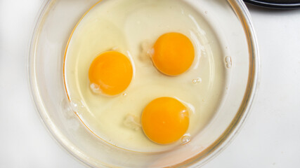 three broken eggs for making French omelet in a glass bowl before whipping