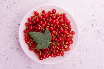
A lot of red currant berries in a plate on a white background. Top view.