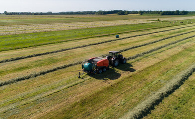 Schwarzer Treker mit einer roten Stroh Festkammerpresse bei der Strohernte auf einem gemähten Feld