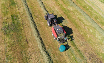 Schwarzer Treker mit einer roten Stroh Festkammerpresse bei der Strohernte auf einem gemähten Feld