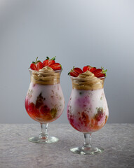 Cold summer dessert. Bowls of layered jelly served on table against light background. Colourful, festive cocktail with sweets jelly in glass. Strawberries, yogurt and chocolate cream close-up.