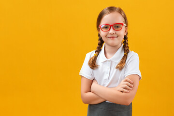 Cute girl schoolgirl in glasses with arms crossed. Portrait of a child on a colored yellow background