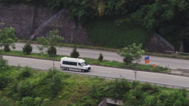 Travel minibus driving on turkish autobahn through mountains / White bus fast speed moving on two sided highway. Aerial drone wide shot at summer sunset