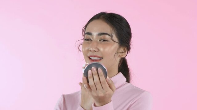 Beauty concept. An Asian woman is making up on the pink background. 4k Resolution.