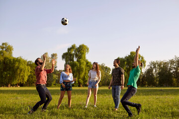 Group of friends having fun playing with a ball on a grass picnic in a summer park.