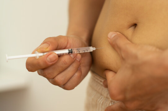 Woman with syringe inject insulin to her belly - diabetes concept, injection