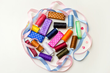 Fototapeta premium Sewing kit. Composition with threads and sewing accessories on a white background, an even layer. Colored satin ribbons