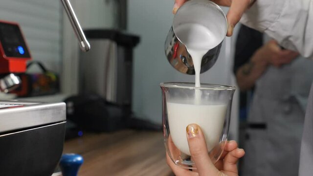 Coffee making proccess. Barista cooking coffee and pours thick and fresh hot milk into transparent mug. Close-up shot of barista pouring milk To make Latte. Slow motion. Full hd