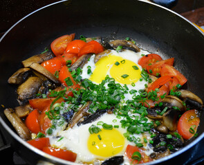 fried eggs with mushrooms and tomatoes, sprinkled with green onions in a pan