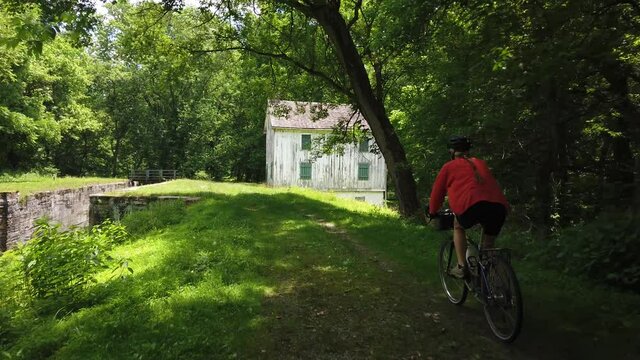 Woman cyclist on C&O canal biking past an old lock house in slow motion.