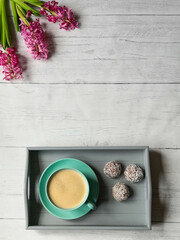Fototapeta na wymiar Cup of coffee and chocolate truffles on gray tray with hyacinth flowers on wooden surface. Top view, from above, flat lay, copy space.