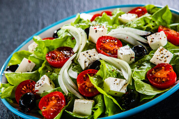 Fresh Greek salad - feta cheese, cherry tomatoes, lettuce, black olives and onion on black stone board
