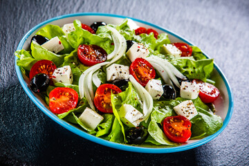 Fresh Greek salad - feta cheese, cherry tomatoes, lettuce, black olives and onion on black stone board
