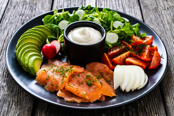 Breakfast - smoked salmon, avocado, garlic creamy dip and vegetable salad on wooden table
