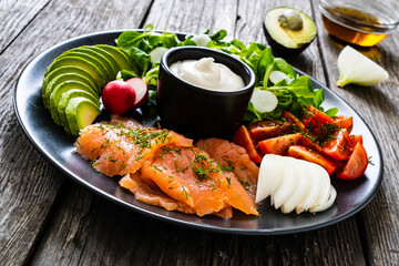 Breakfast - smoked salmon, avocado, garlic creamy dip and vegetable salad on wooden table
