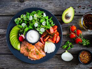 Breakfast - smoked salmon, avocado, garlic creamy dip and vegetable salad on wooden table
