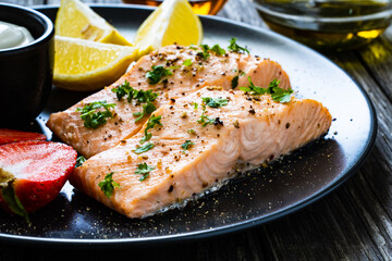 Steamed salmon steaks with lemon, strawberries and creamy dip served on black plate on wooden table
