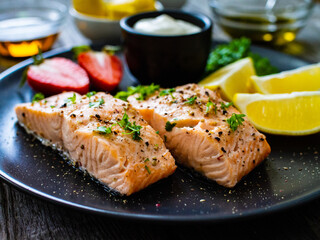 Steamed salmon steaks with lemon, strawberries and creamy dip served on black plate on wooden table
