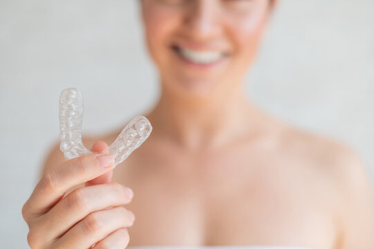 Close-up of orthodontic silicone transparent teeth aligner in female hands. Blurred unrecognizable woman holds a removable night retainer. Bracket for teeth whitening for a perfect smile.