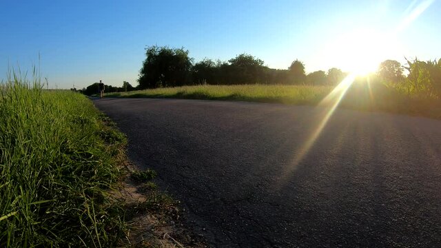 Person walking down a rural road in summer during a beautiful sunset (front-view)