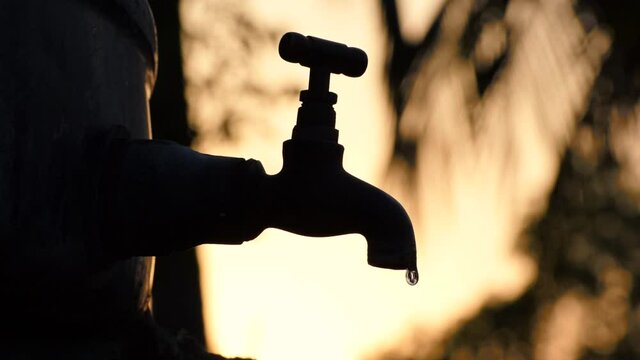 Silhouette footage of old vintage metal tap leaking water drops. alone in outdoor natural environment during golden hour of summer sunrise, water shortage , crisis , scarcity , save water