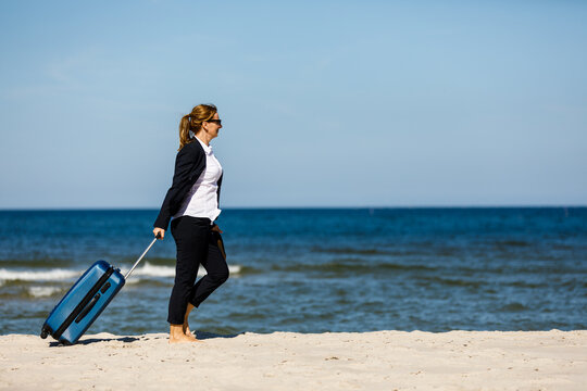 Businesswoman walking with suitcase on beach

