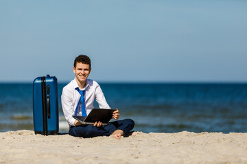 Businessman with laptop and suitcase relaxing on beach
